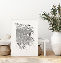 Load image into Gallery viewer, A black and white illustrated map of Palmerston North laid out on white paper within a white frame, leaning against a white bench seat and wooden flooring.