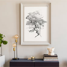 Load image into Gallery viewer, A black and white illustrated print of Cambridge laid out on white paper within a big white frame hung on an off white wall, above a console with a lamp and books.