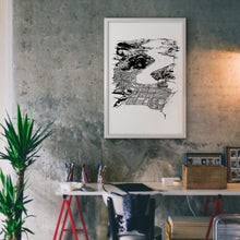 Load image into Gallery viewer, A black and white illustrated print of Dunedin City laid out on white paper framed in a white frame hung on a concrete wall above a desk setting