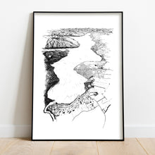 Load image into Gallery viewer, A black and white illustrated print of Te Anau laid out on white paper, framed in a black frame, leaning on a white wall and wooden flooring.