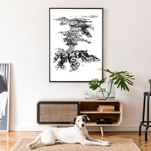 Load image into Gallery viewer, A black and white illustrated print of Waiheke Island laid out on white paper within a black frame hanging on a white wall above a modern console with a dog lying below.